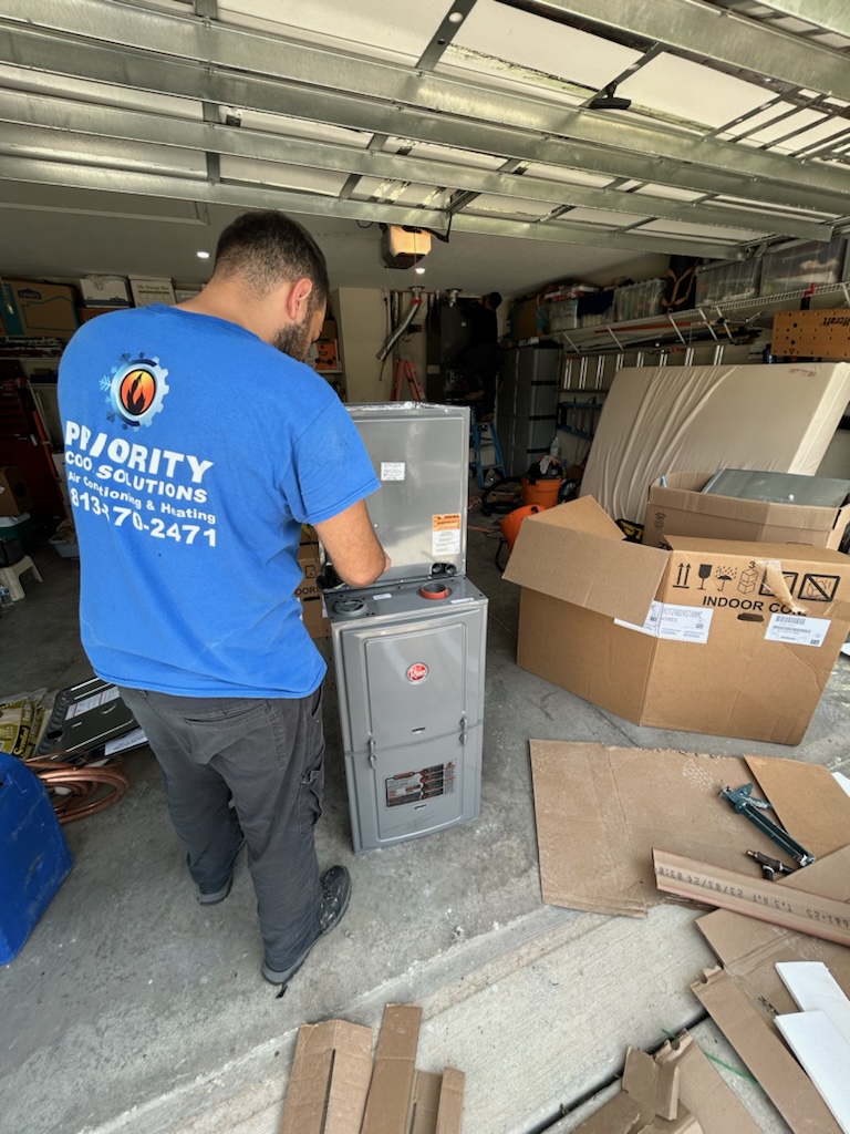 Technician installing HVAC system in a garage wearing a Priority HVAC Solutions shirt.