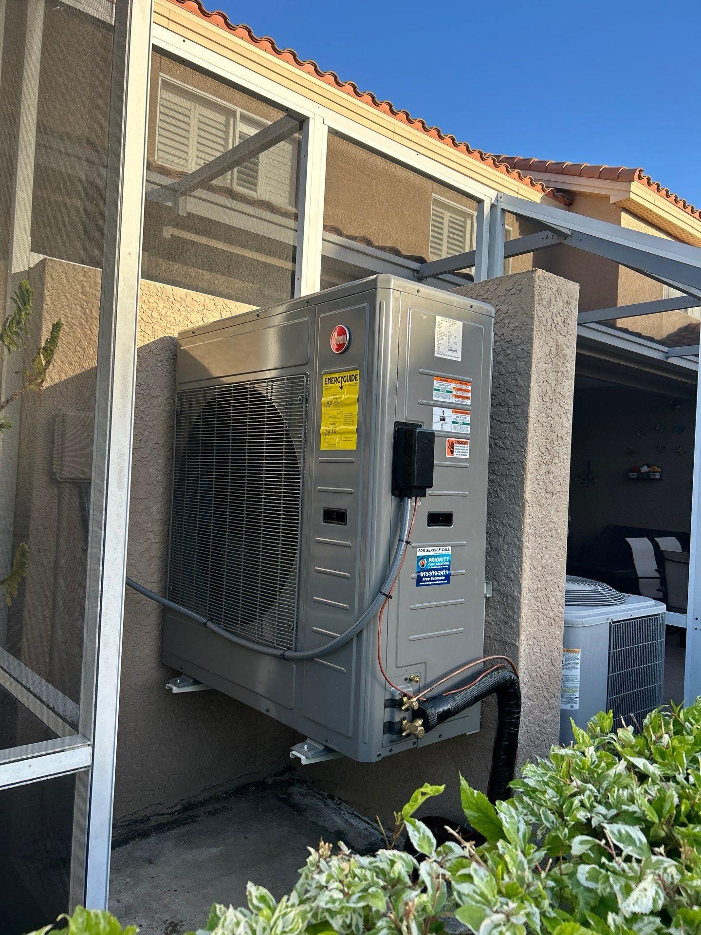 Rheem heat pump installed outside a house with energy guide label visible.
