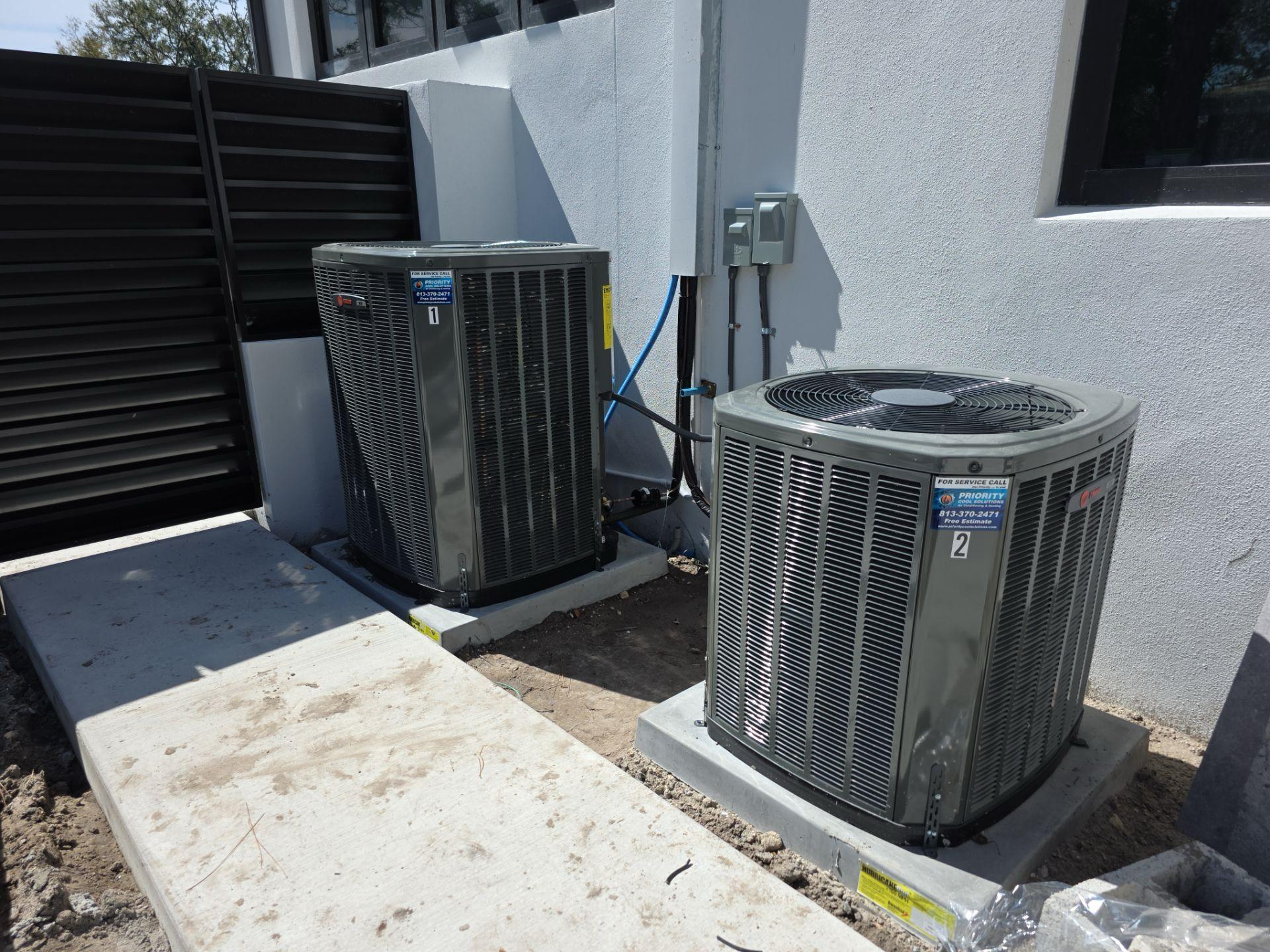 Two outdoor air conditioning units next to a building on a concrete pad.