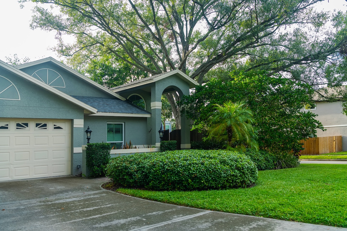 Front view of a house with gray exterior, garage, and lush greenery in the yard.