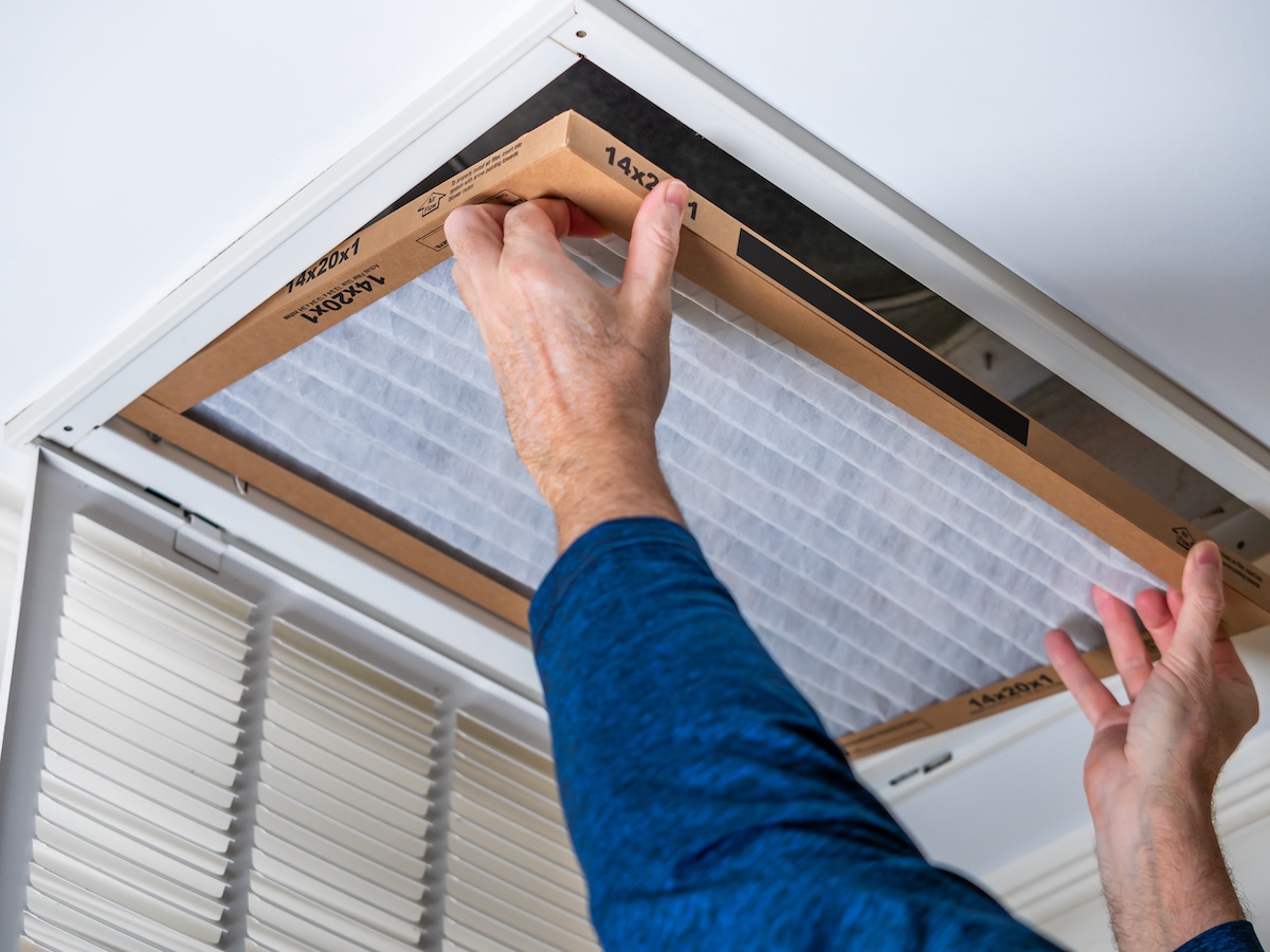 Person changing air filter on ceiling vent for home maintenance.