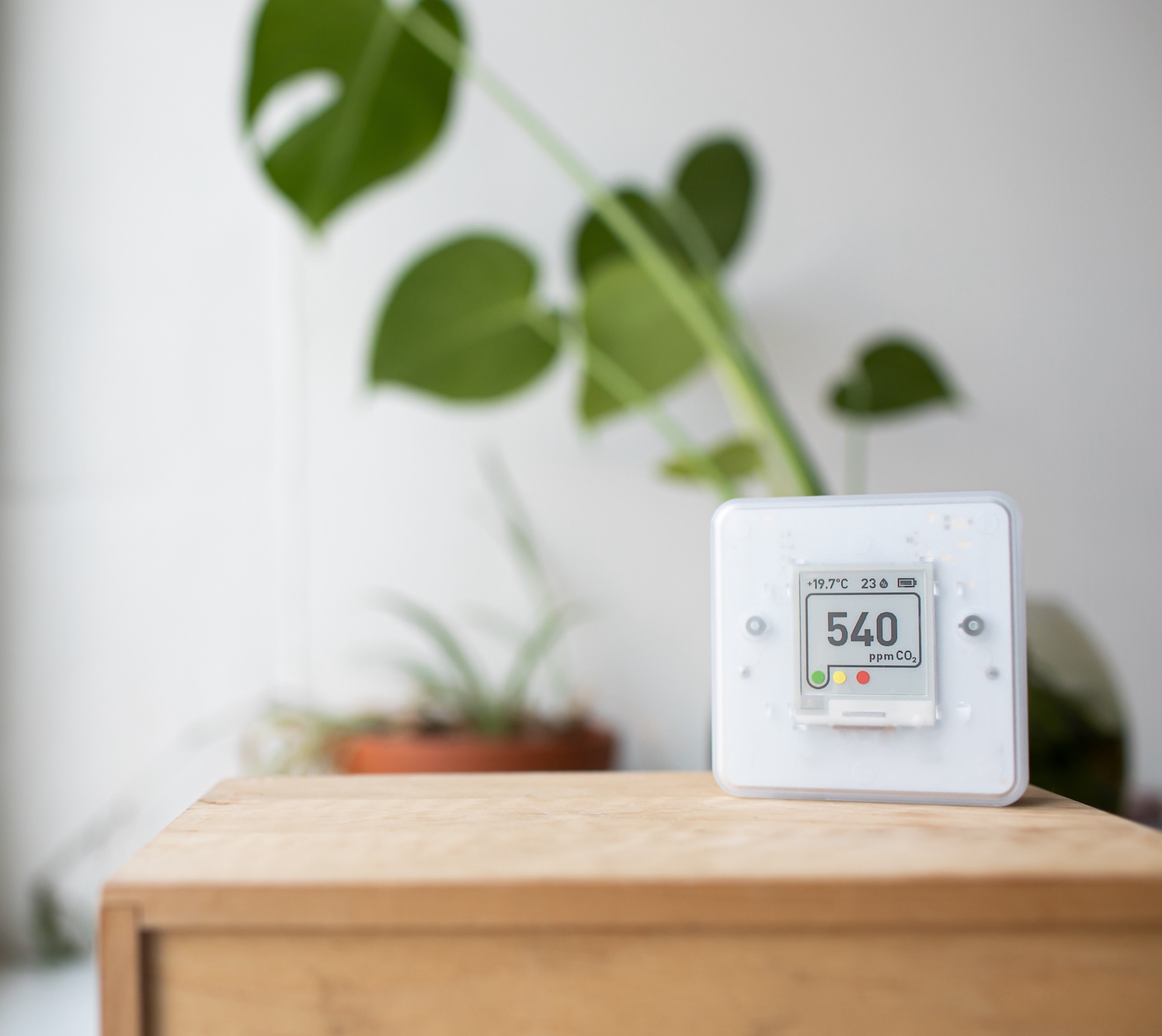 CO2 sensor displaying 540 ppm with temperature in a room with houseplants in the background.