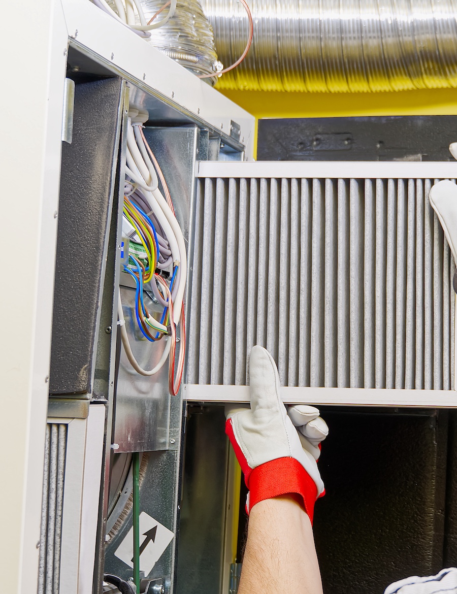 Replacing a furnace filter with red and white gloves in an HVAC system.