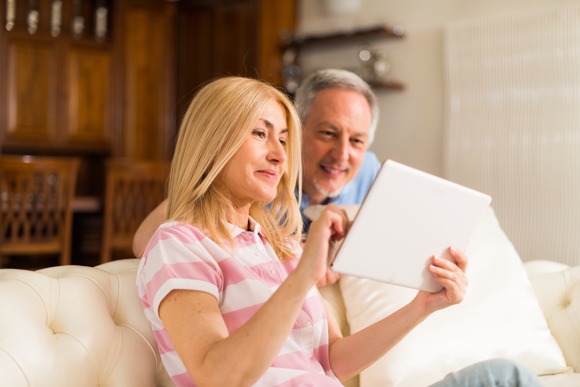 A woman and man smiling while using a tablet on a couch in a cozy living room.
