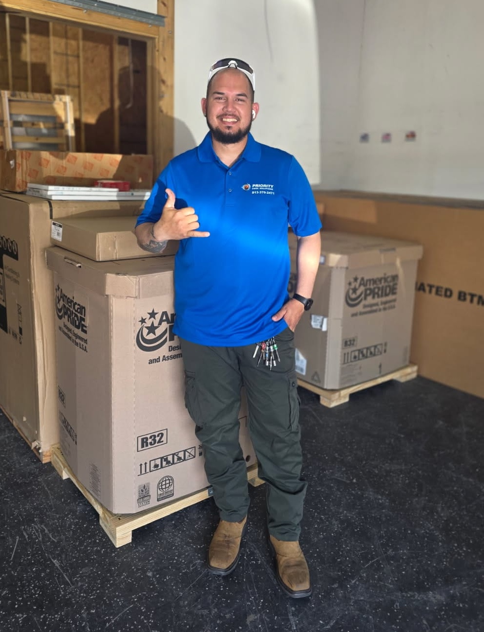 Man in blue shirt posing with large boxes in a warehouse setting.
