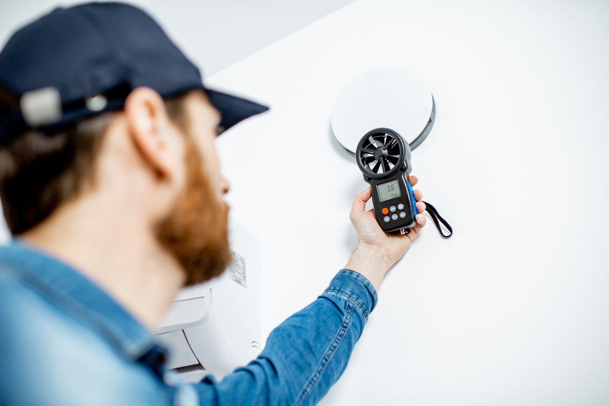Technician using an anemometer to measure airflow near a ceiling vent.