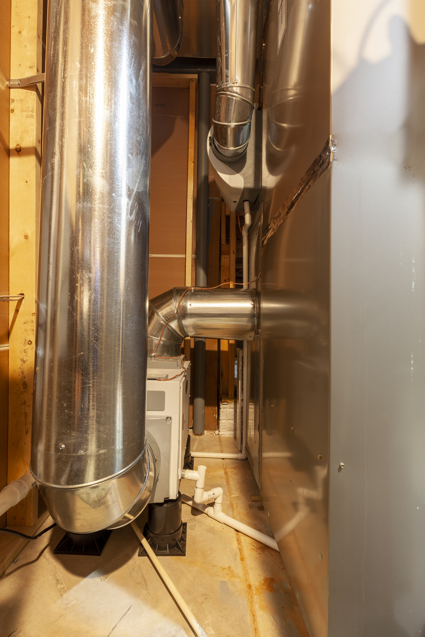 Industrial HVAC system with metal ducts and piping in a mechanical room setting.