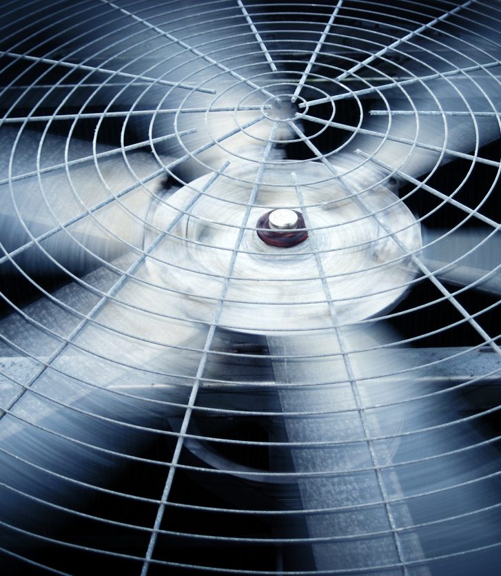 Spinning industrial fan blades with protective metal grille in motion.