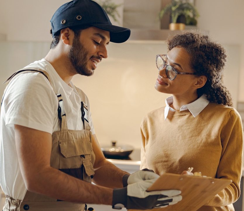 A worker in uniform showing a clipboard to a woman in glasses at home.