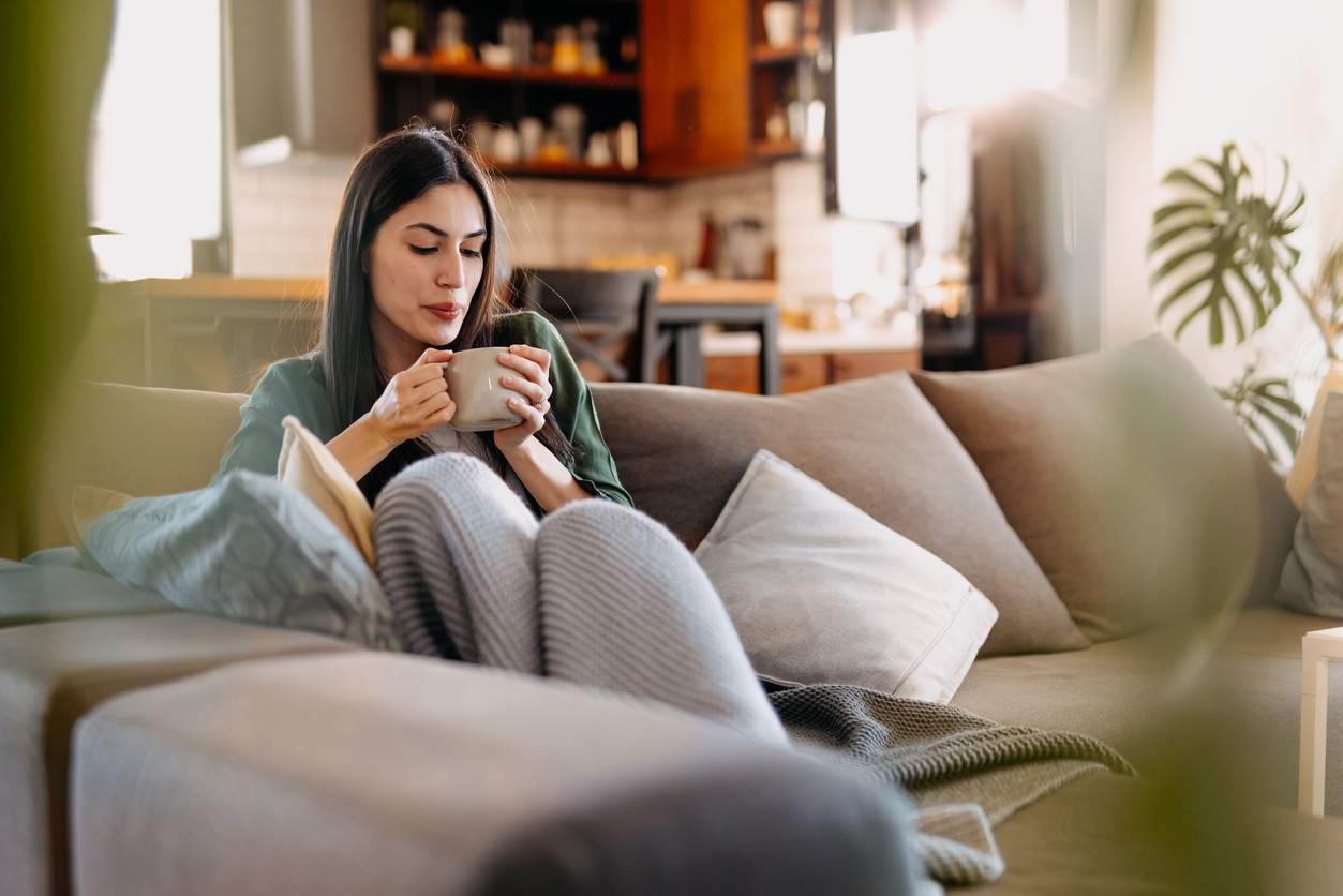 Woman relaxing on a cozy couch, sipping coffee in a comfortable living room setting.