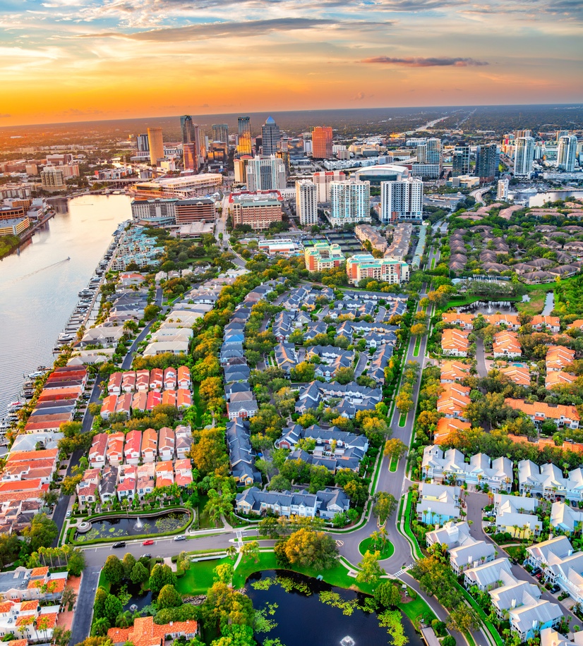 Aerial view of a vibrant cityscape at sunset with buildings, river, and lush greenery.