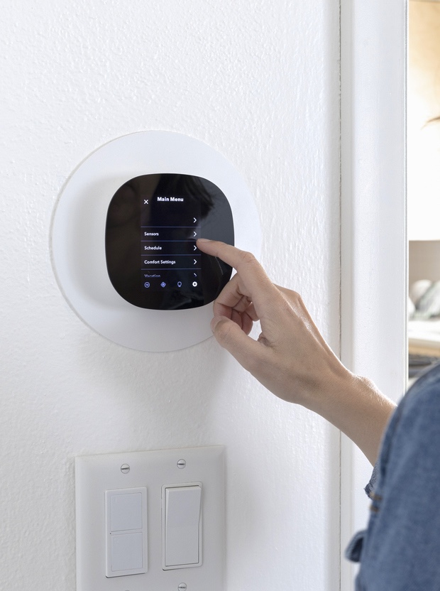 A person adjusting a smart thermostat on a wall next to light switches.