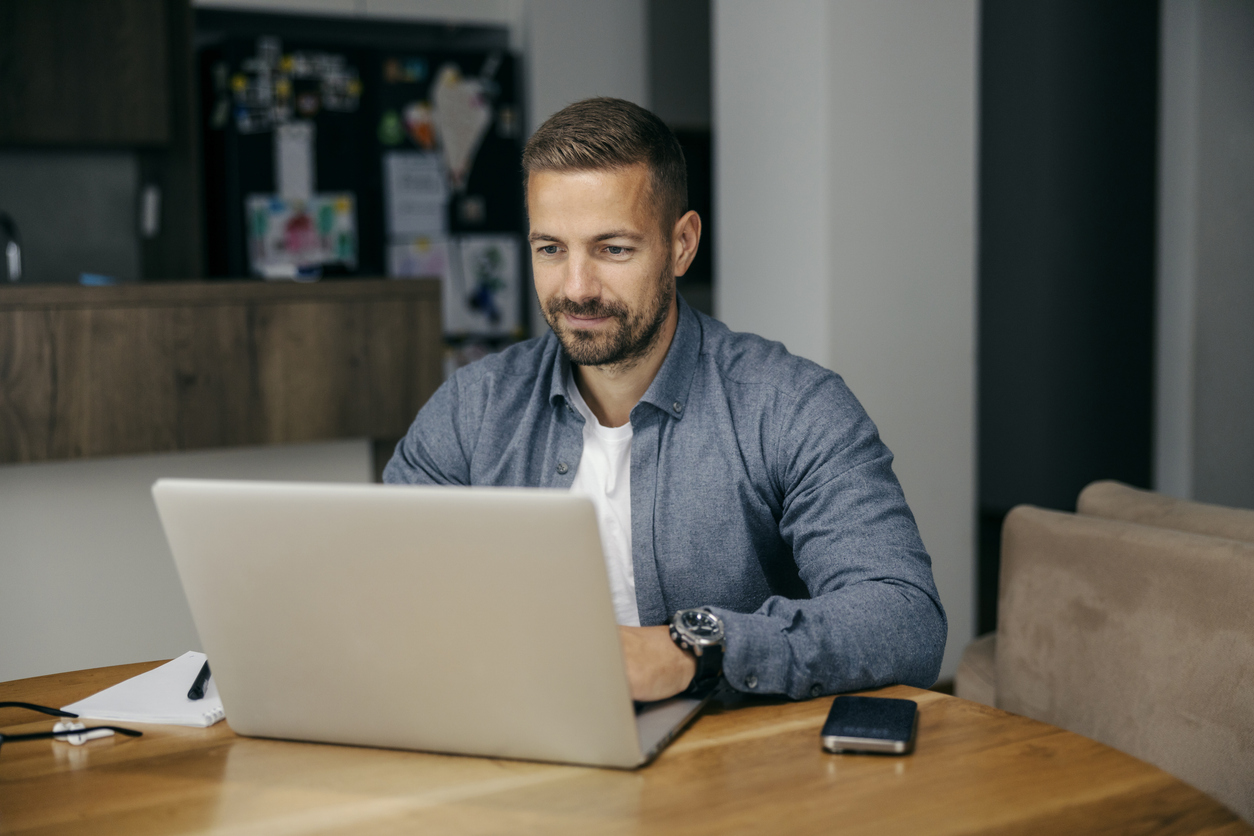 A man using a laptop at a wooden table in a cozy home setting.