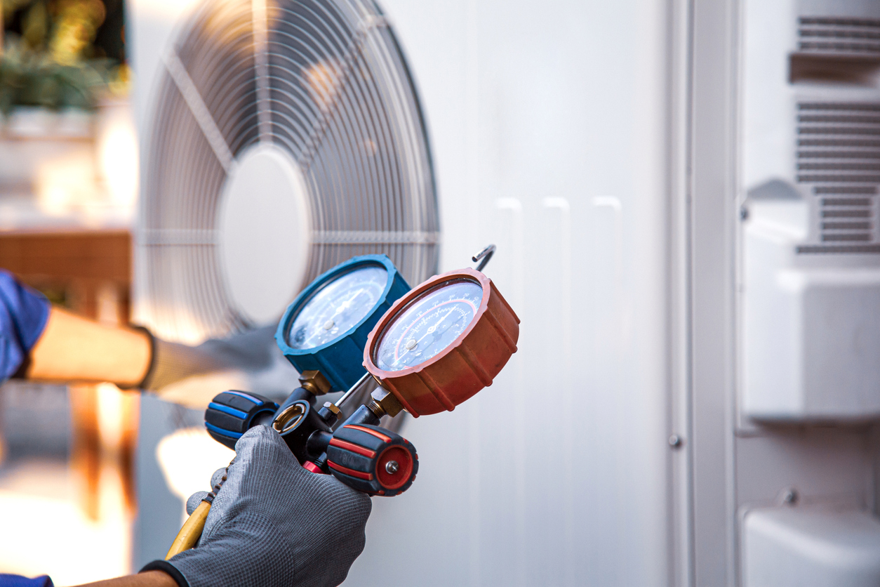 AC technician using pressure gauge to test and repair outdoor HVAC unit.