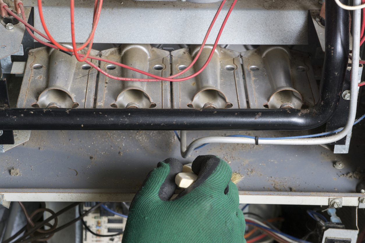 Technician cleaning a furnace igniter with wires and components visible.